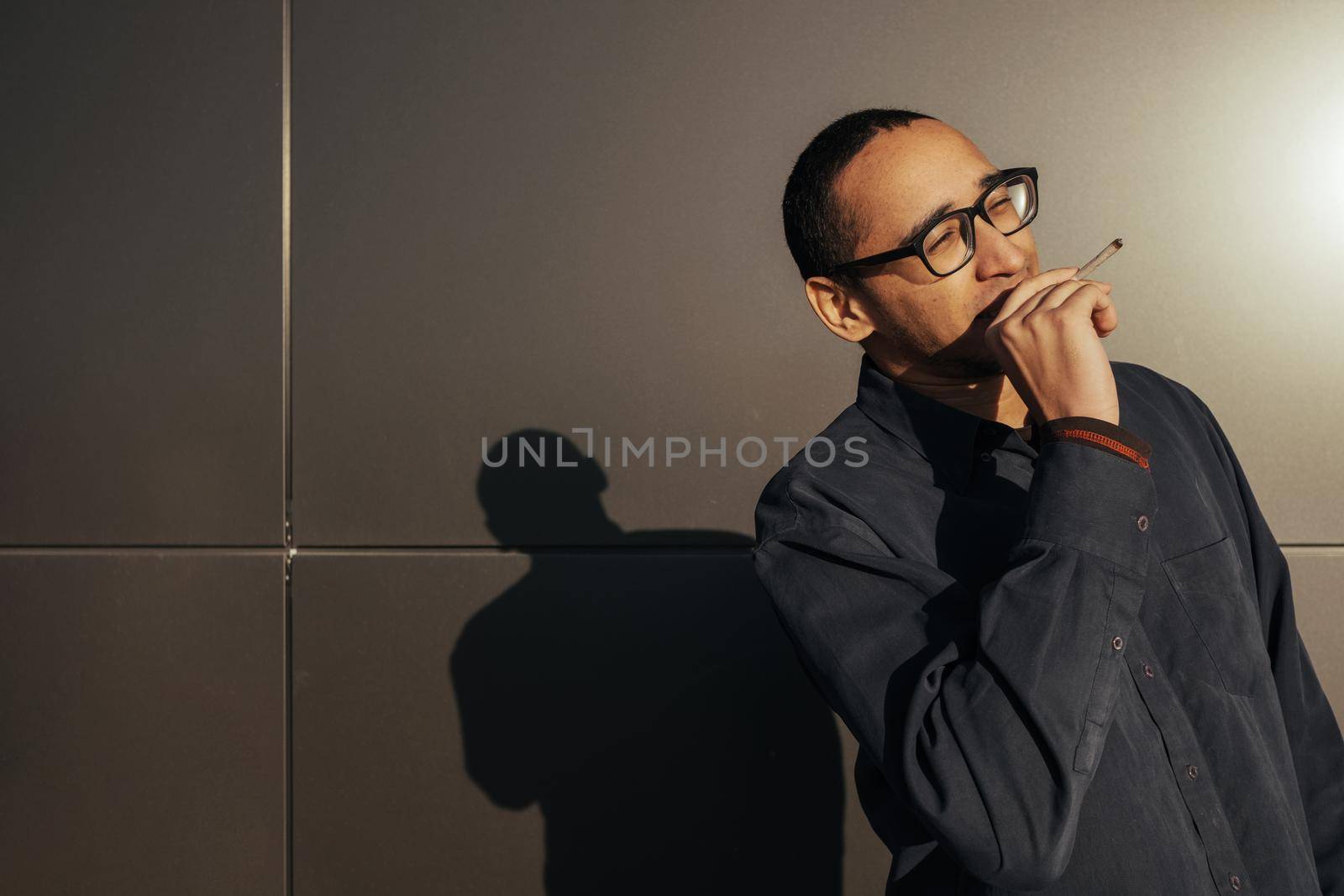 Man smoking a white paper joint close up. Sungles black background