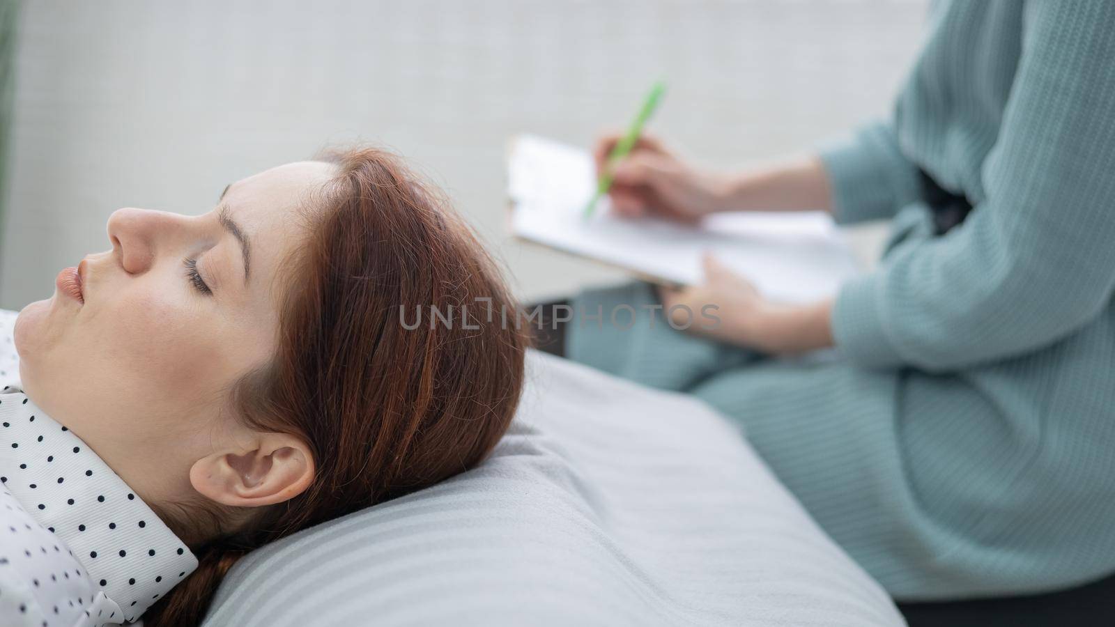 A caucasian woman lies on a couch and expresses her feelings, while a psychologist makes notes on a tablet. by mrwed54