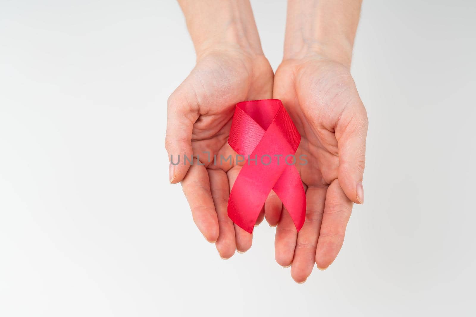 Female hands with a red ribbon on a white background. Symbol of the fight against AIDS. Copy space