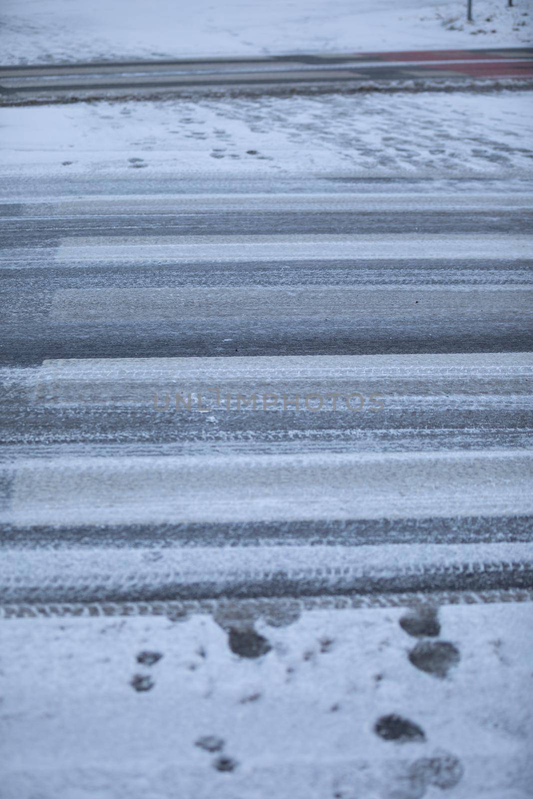 Uncleared street and pedestrian crossing of snow and frozen ice. More dangerously slippery at the pedestrian crossing.