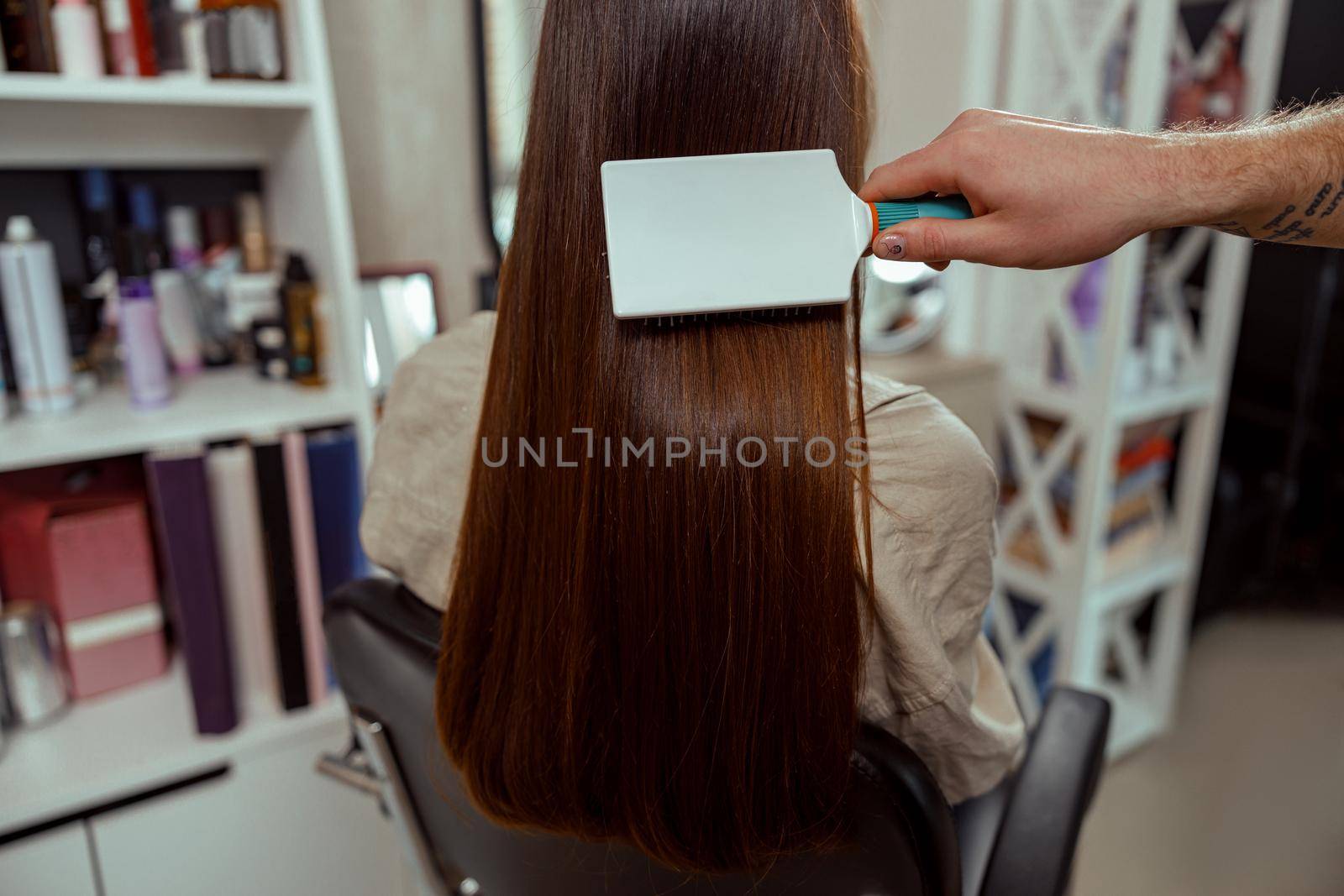 Closeup of hairstylist brushing long and sleek brown hair of female client at beauty salon.