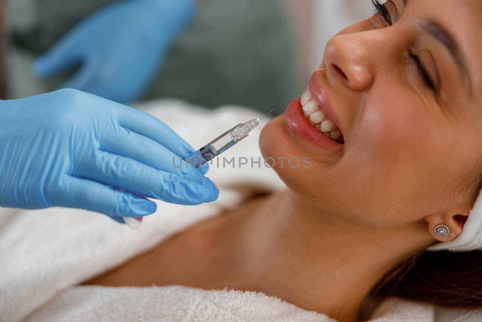 Smiling young woman getting hyaluronic acid injections in lips at beauty salon. Cosmetology