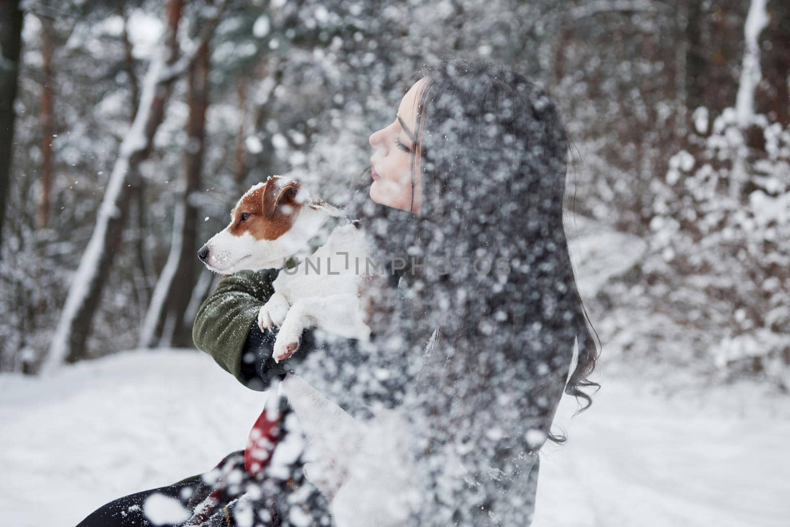 It's snowfall. Smiling brunette having fun while walking with her dog in the winter park by Standret