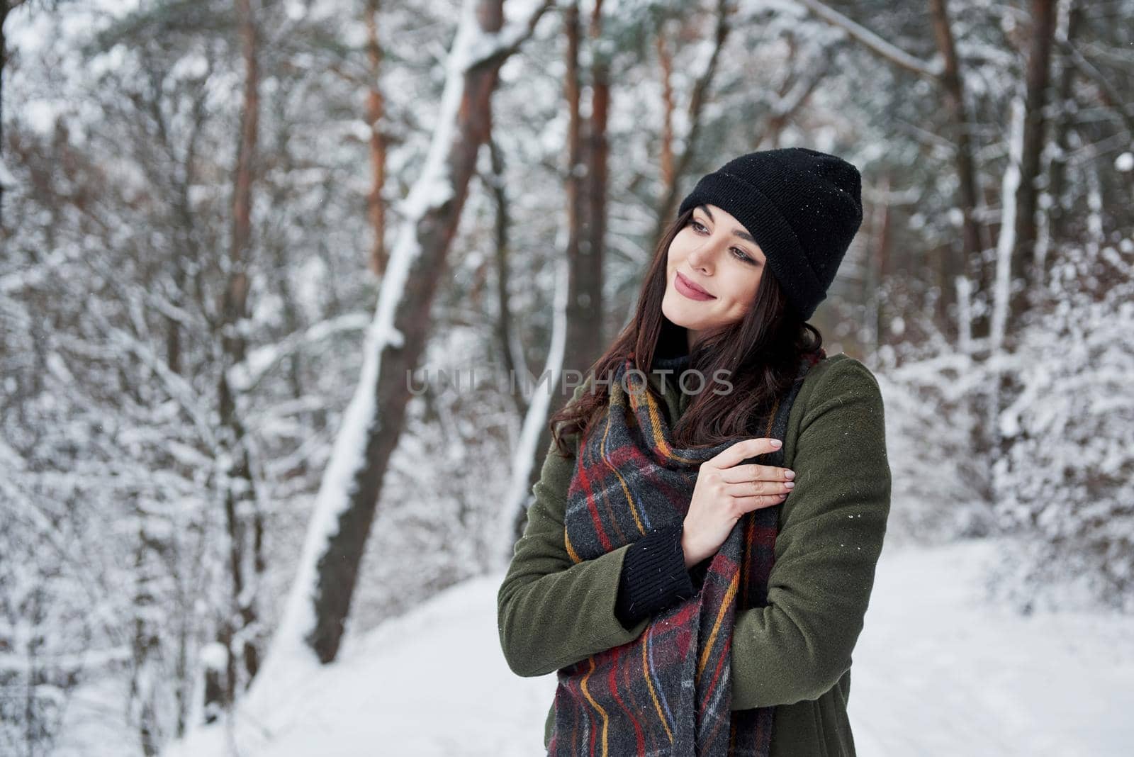 Feeling joy. Cheerful young girl in warm clothes have a walk in the winter forest at daytime.