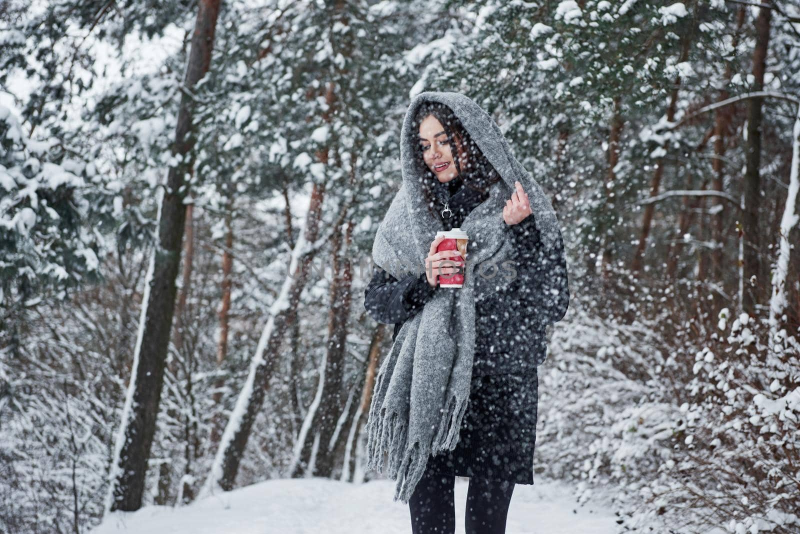 Nice landscape at background. Girl in warm clothes with cup of coffee have a walk in the winter forest.