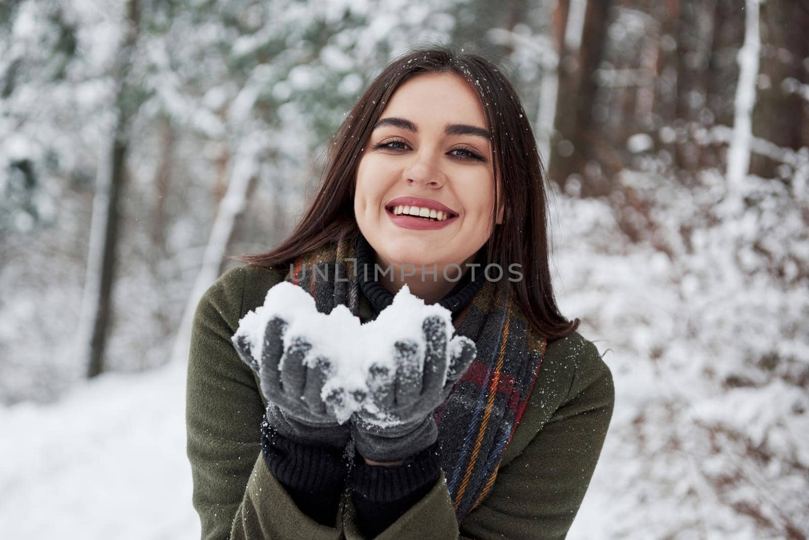 Happy brunette holding snow in hands and smiling. Winter forest.