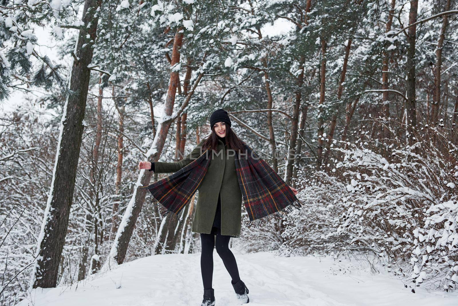 Well dressed for that season. Cheerful young girl in warm clothes have a walk in the winter forest at daytime.