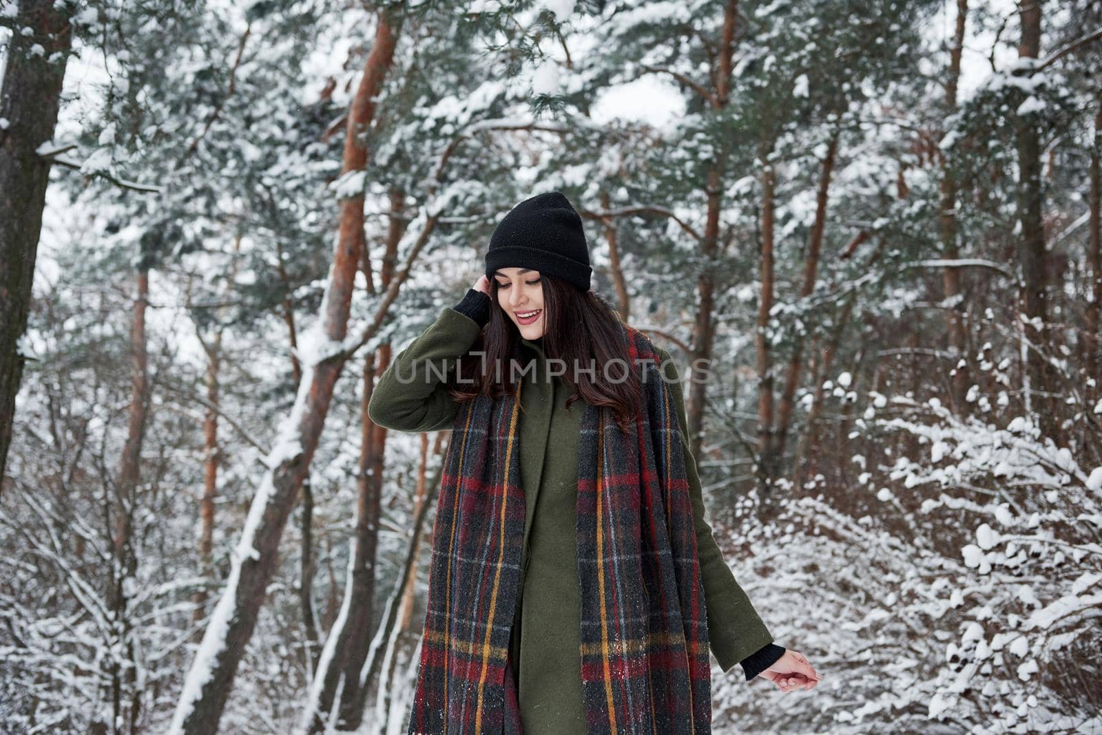 Holidays season. Cheerful young girl in warm clothes have a walk in the winter forest at daytime.