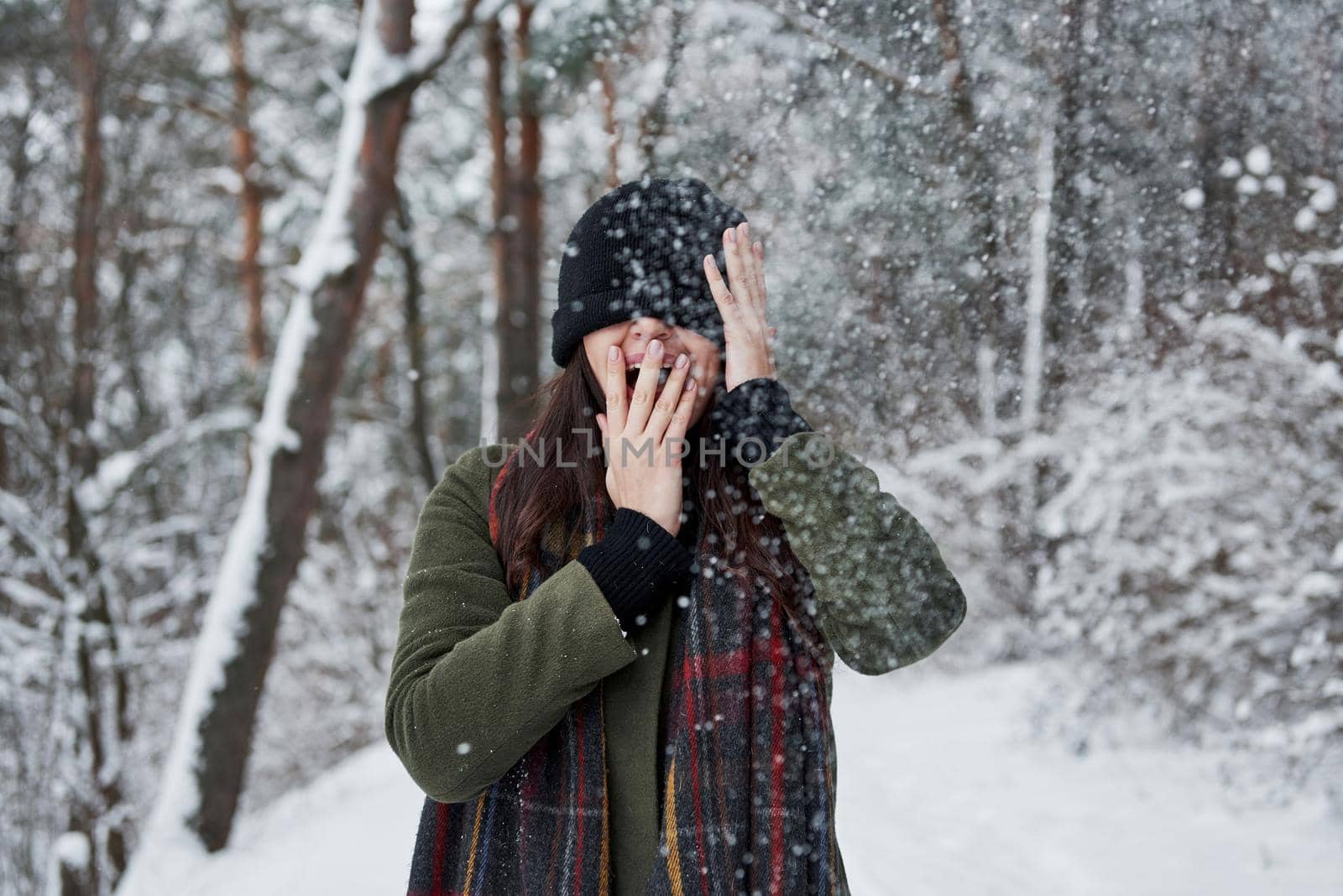 Black cap is covering the eyes. Touching the face. Cheerful young girl in warm clothes have a walk in the winter forest at daytime.