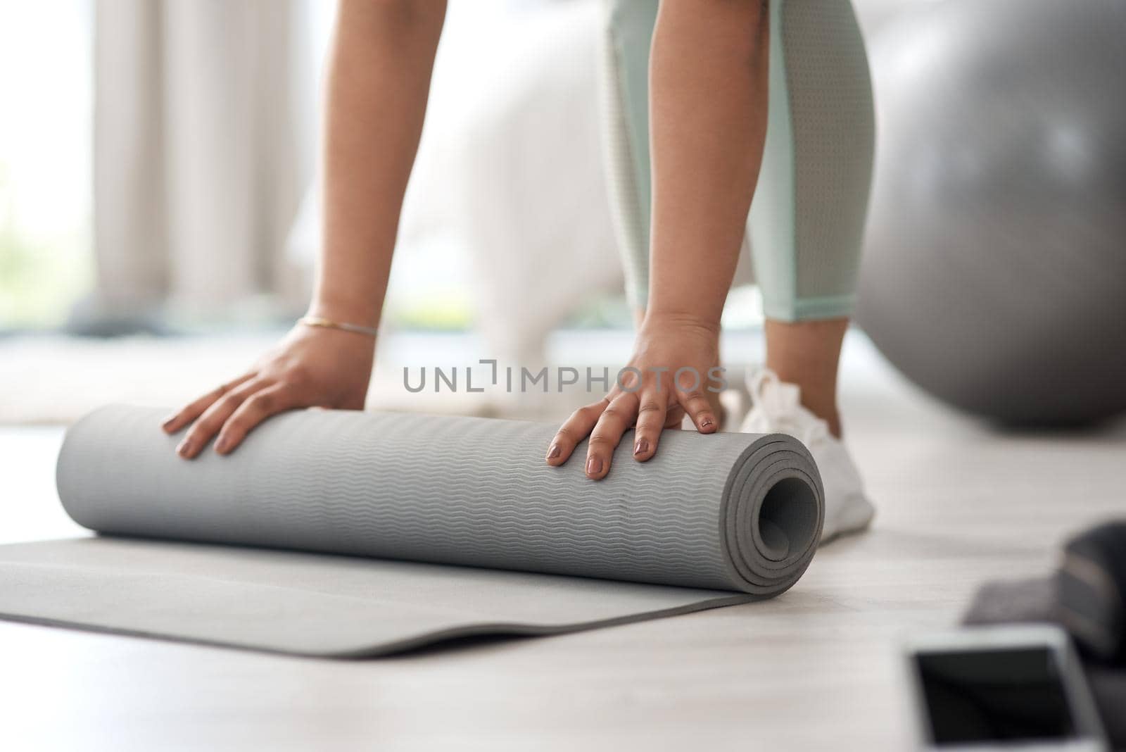 Closeup shot of an unrecognisable woman rolling an exercise mat on the floor at home.