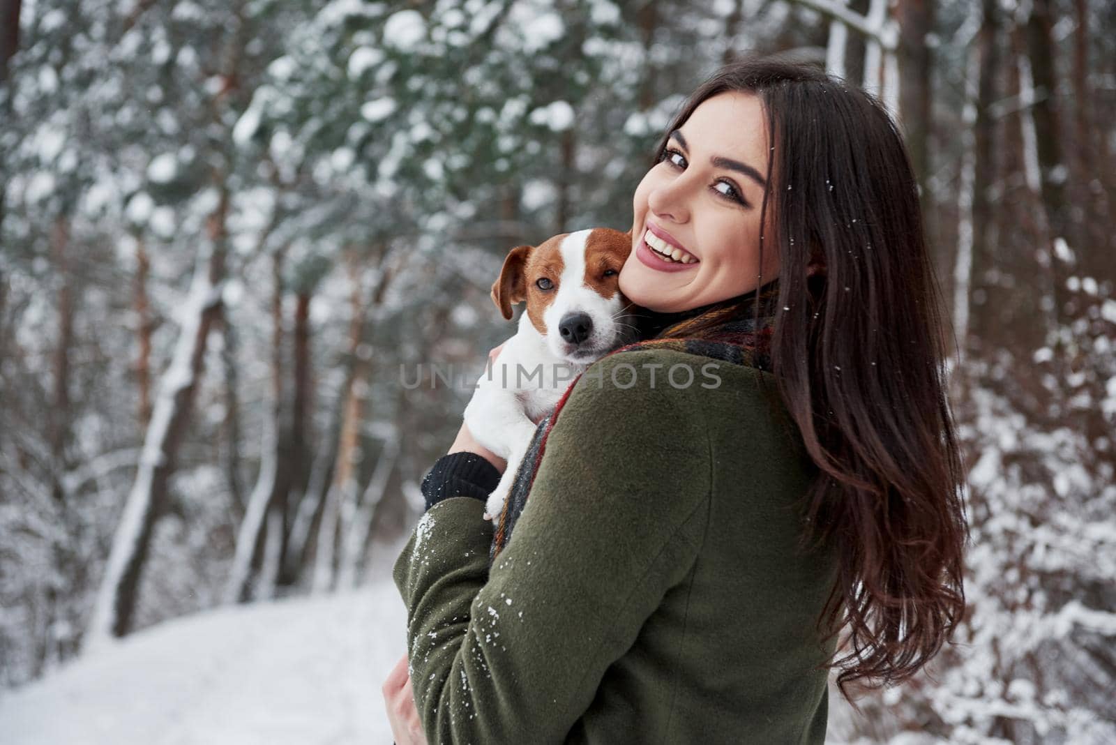 Girl is turned her head to the camera. Smiling brunette having fun while walking with her dog in the winter park.