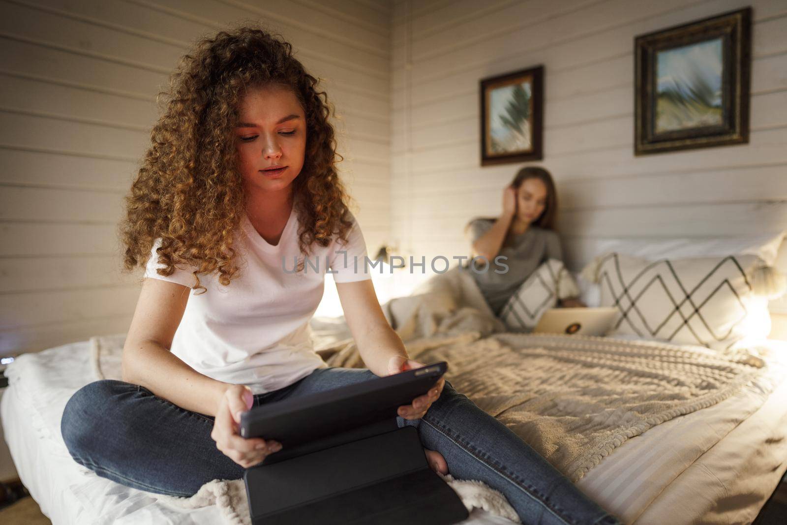 Two beautiful women lying in bed, holding and watching laptop