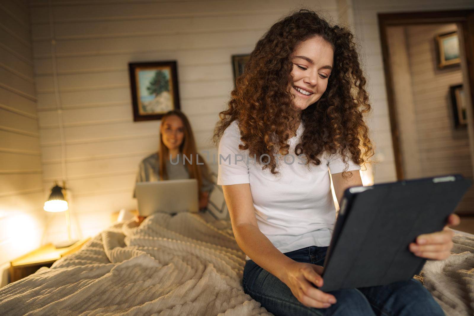 Two beautiful women lying in bed, holding and watching laptop