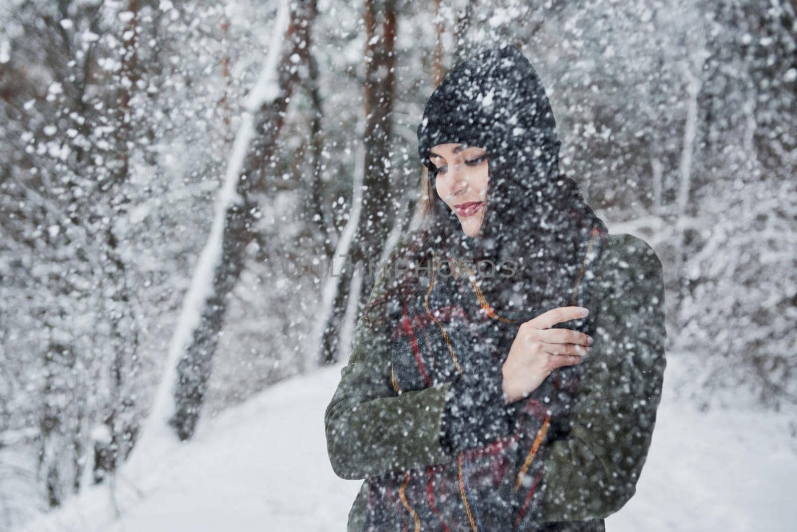 Looks like it's cold there. Cheerful young girl in warm clothes have a walk in the winter forest at daytime.