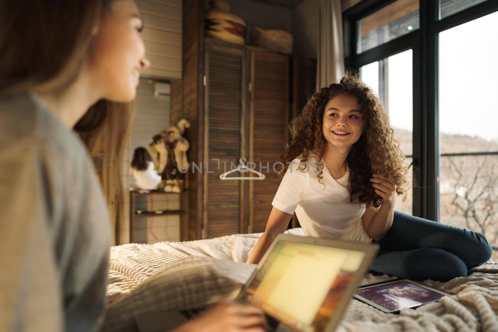 Two beautiful women lying in bed, holding and watching laptop