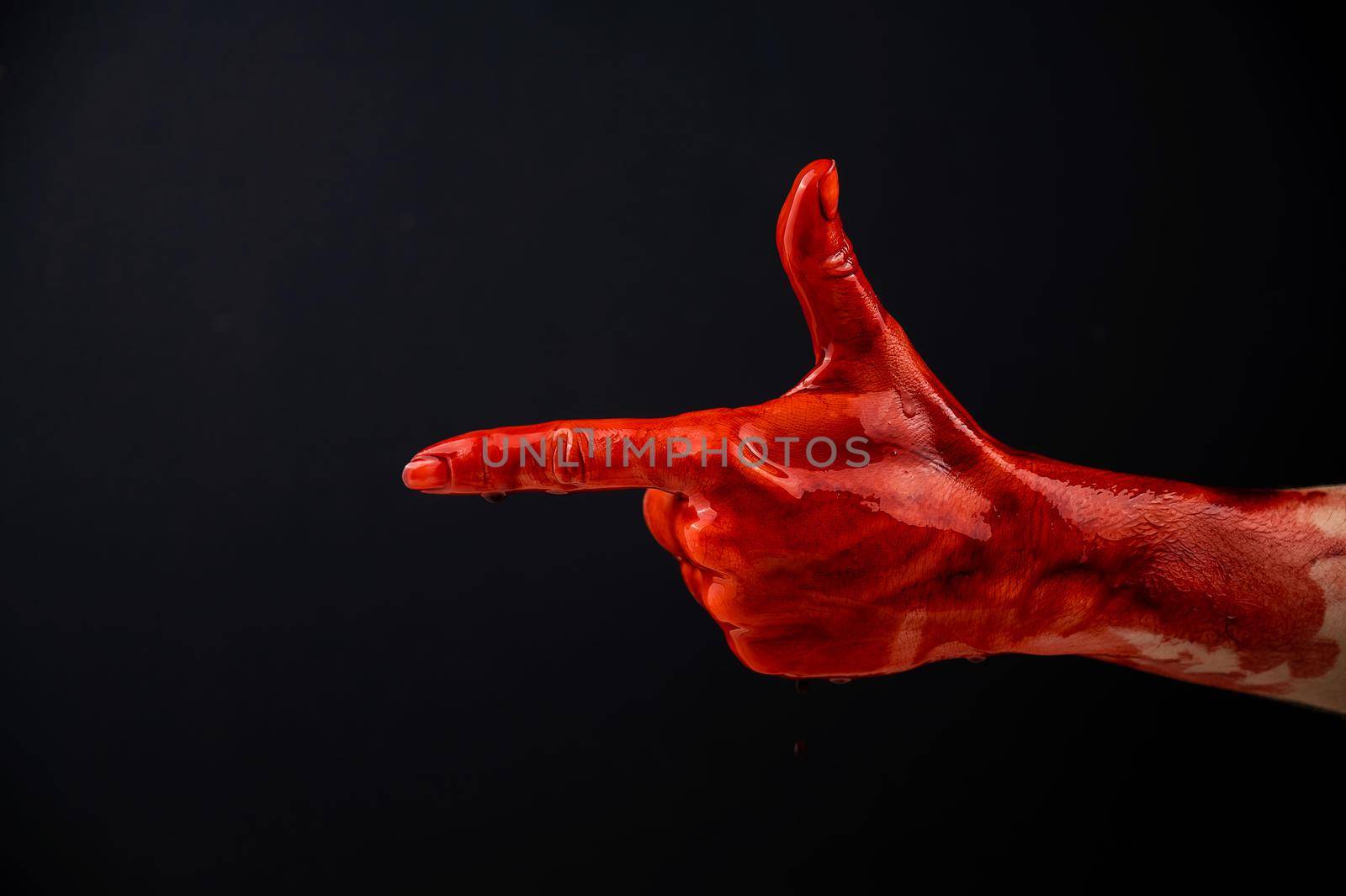 Woman's hand in blood shows a gesture of a gun on a black background