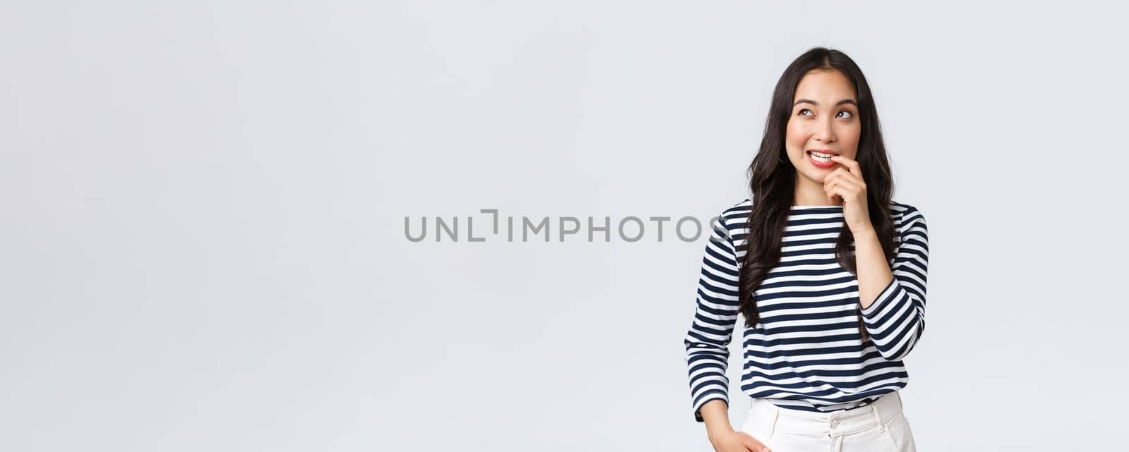 Lifestyle, people emotions and casual concept. Thoughtful, dreamy and creative asian woman having plan, biting finger while pondering, thinking and looking upper left corner focused.
