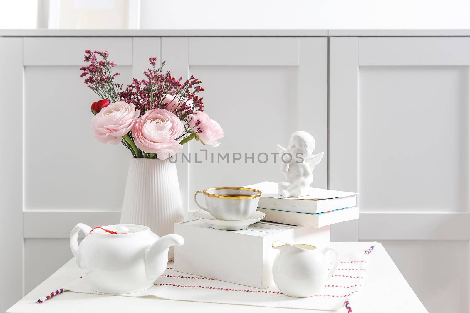 Bouquet of pink Persian buttercups on a white table in front of a chest of drawers. Scandinavian style. Place for text by elenarostunova