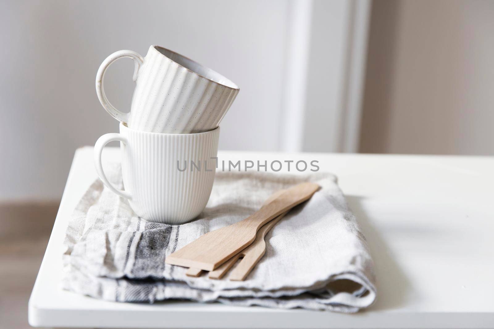 Two white mugs, a kitchen towel, a napkin and wooden frying utensils on the table. Defocus.