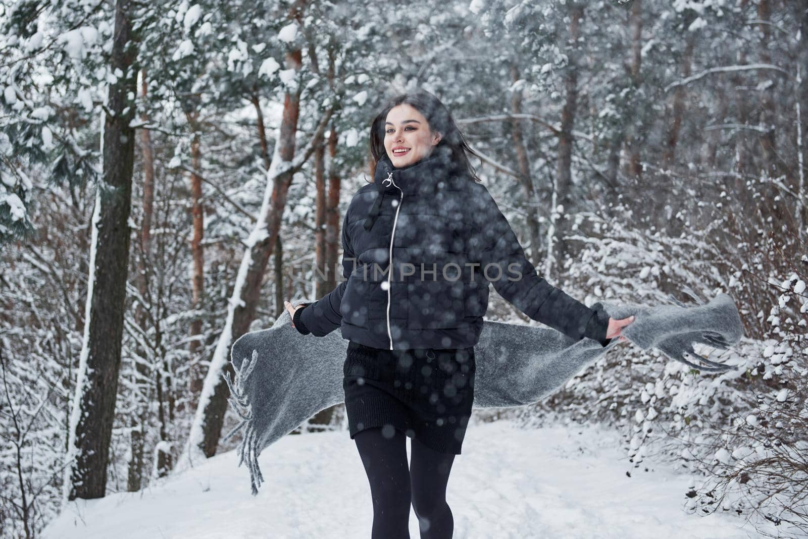 Running forward. Portrait of charming woman in the black jacket and grey scarf in the winter forest.