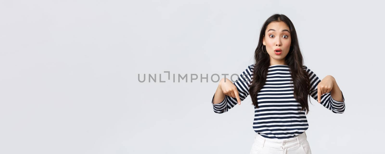 Lifestyle, beauty and fashion, people emotions concept. Amazed excited cute asian woman open mouth and widen eyes fascinated, pointing fingers down as telling about cool event or special discounts.