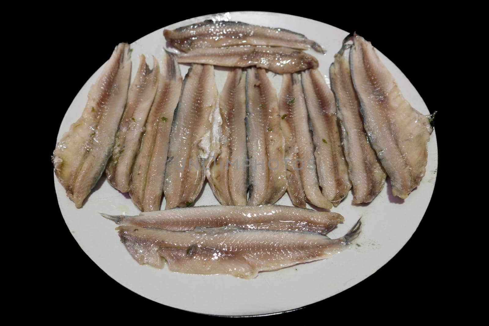 Raw anchovy slices plate over black background