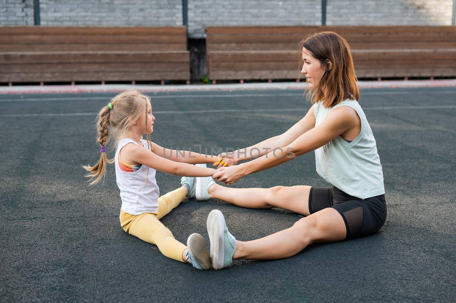 Mother and daughter go in for sports outdoors. Caucasian woman and little girl are engaged in fitness at the stadium. by mrwed54