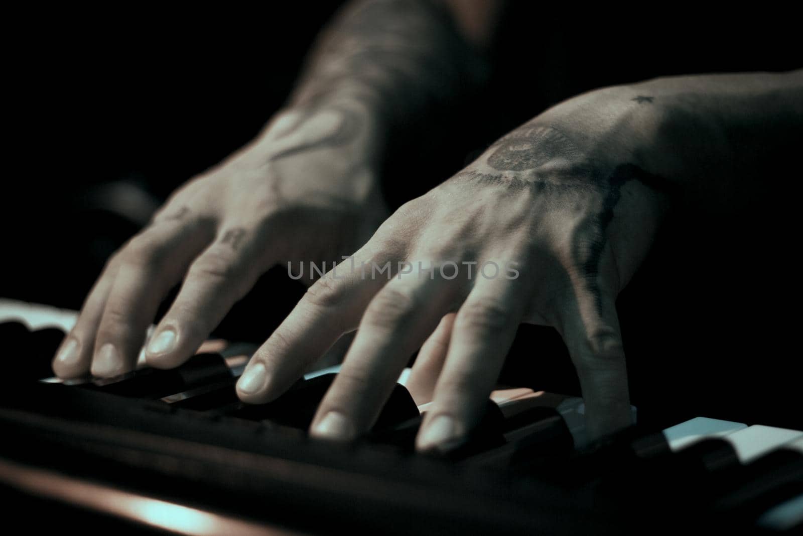 Tattooed mans hands on the keyboard of a piano. Dark background