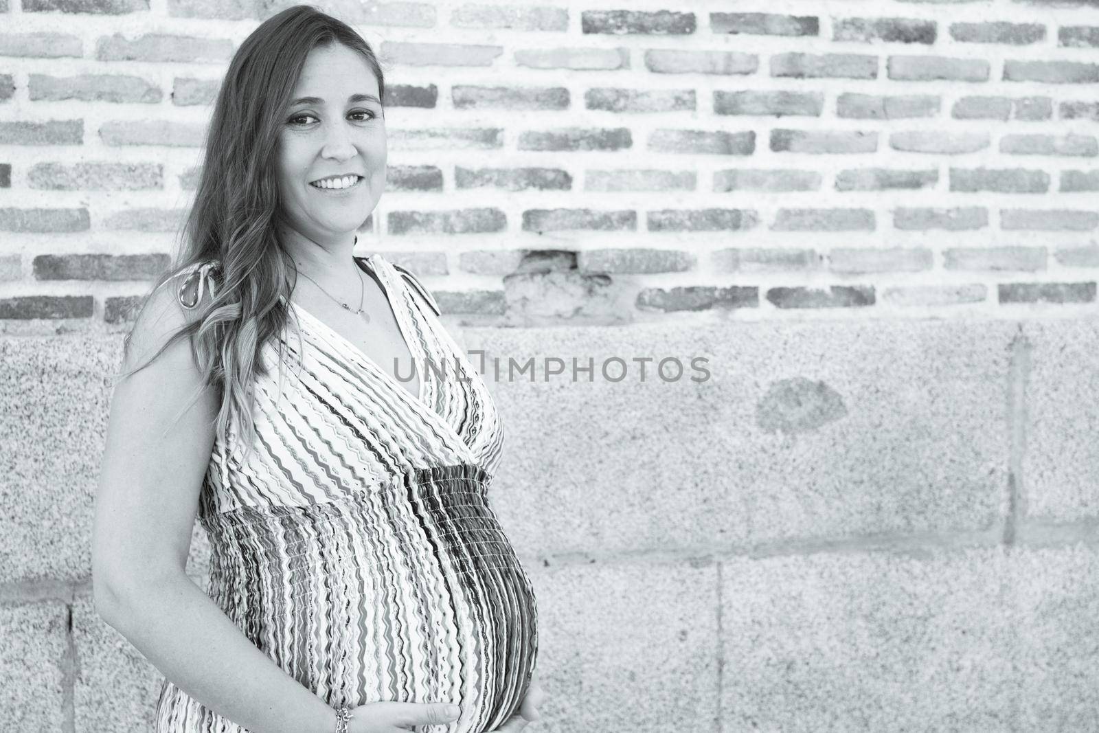 Seven month pregnant woman outdoors in multi colored striped dress. Day scene