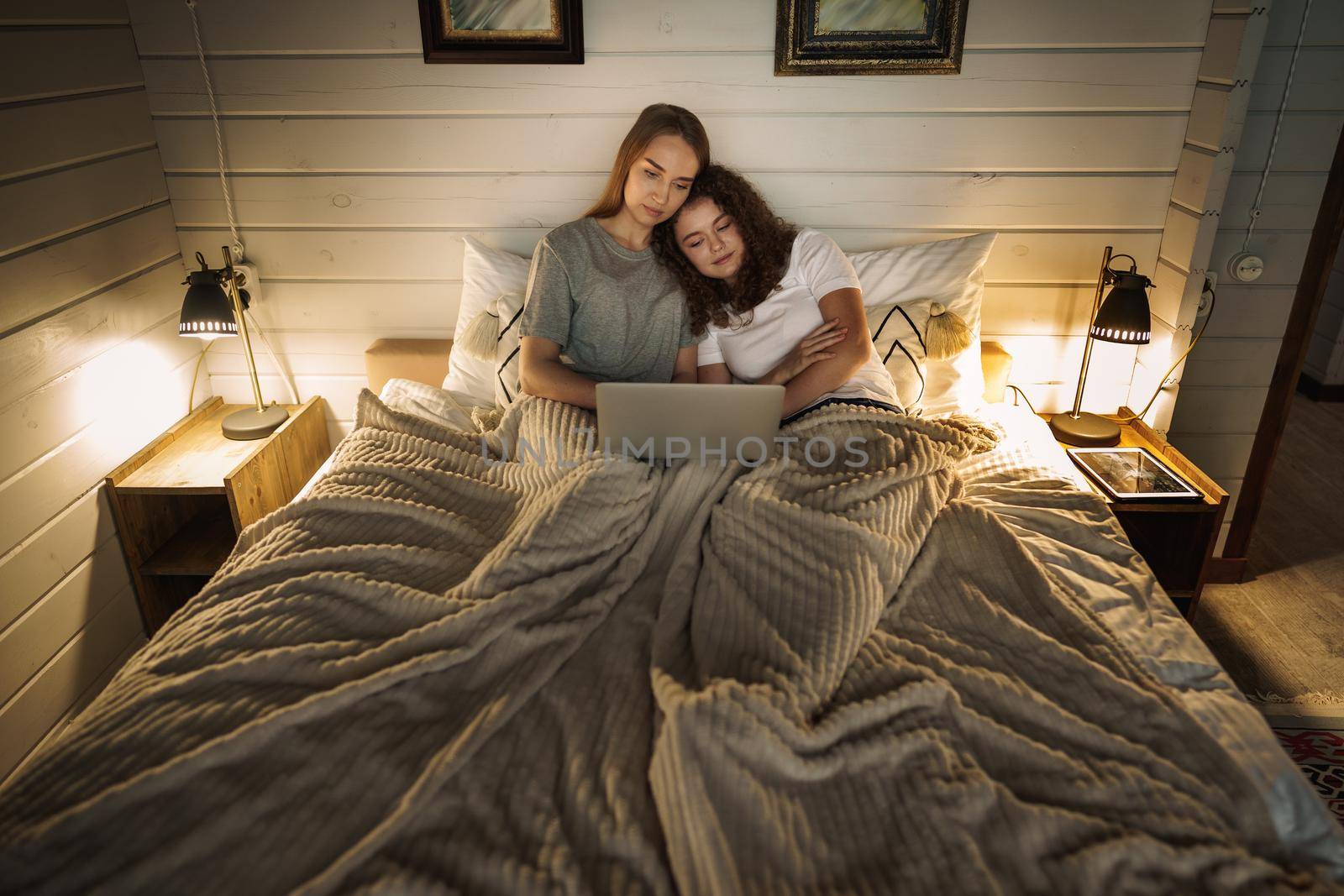Two beautiful women lying in bed and watching movies on laptop at home