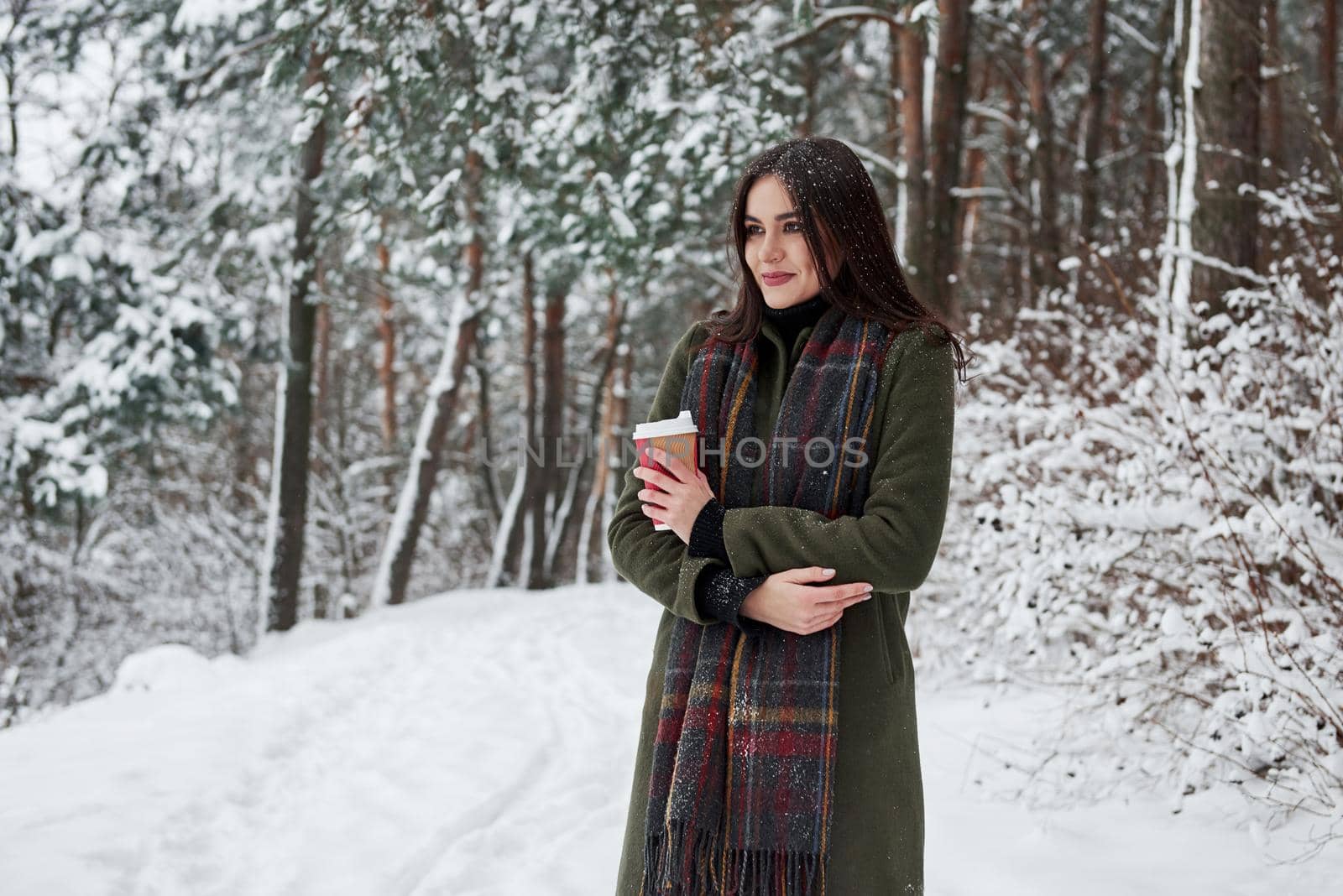 Enjoying beautiful nature. Girl in warm clothes with cup of coffee have a walk in the winter forest.