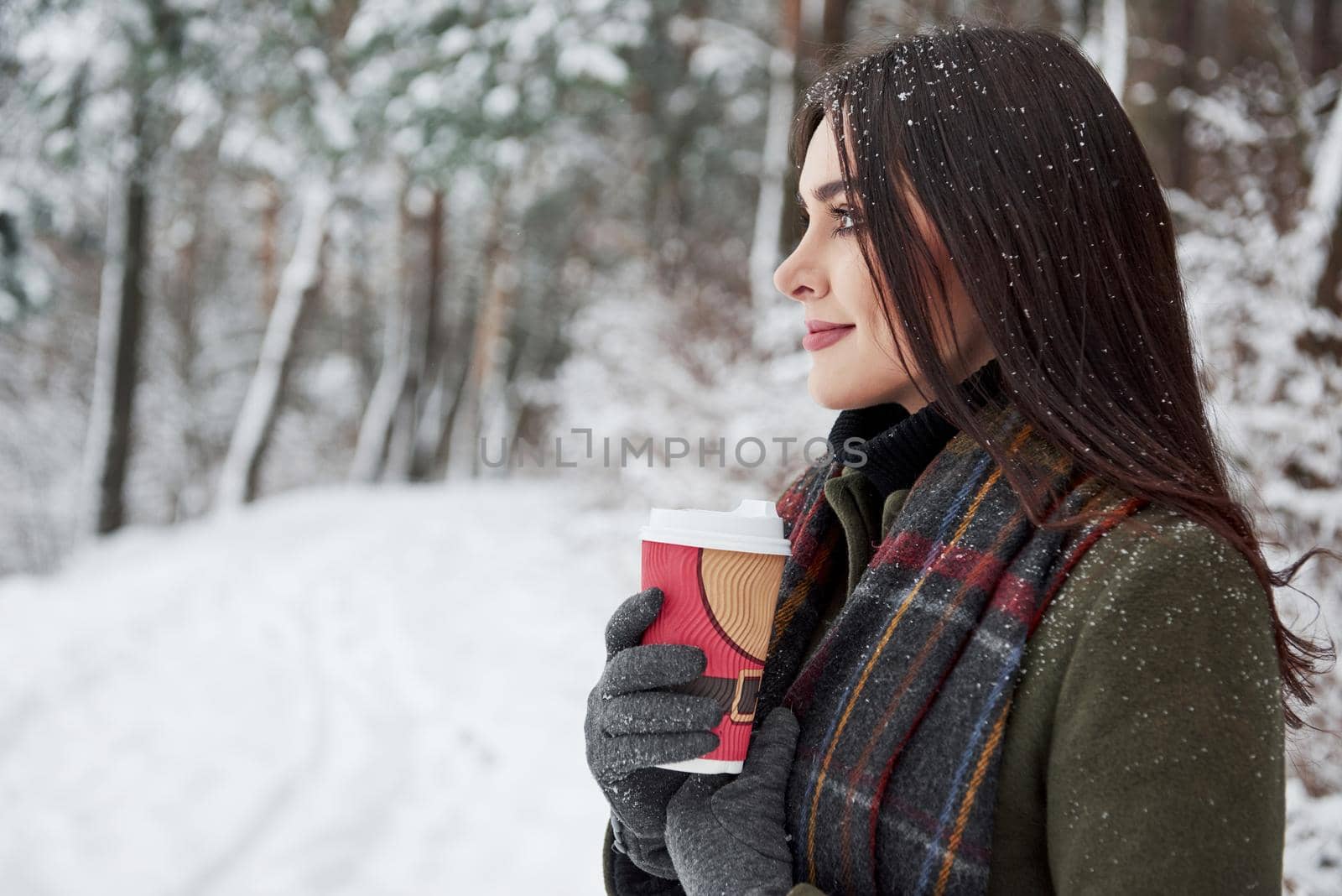 Nice weather. Side view. Girl in warm clothes with cup of coffee have a walk in the winter forest.