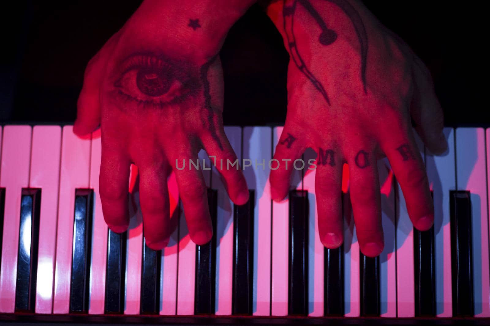 Tattooed mans hands on the keyboard of a piano. Dark background