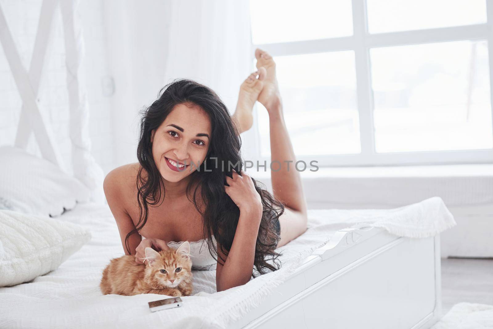Nice portrait. Attractive blonde resting on the white bed with her cute kitten by Standret