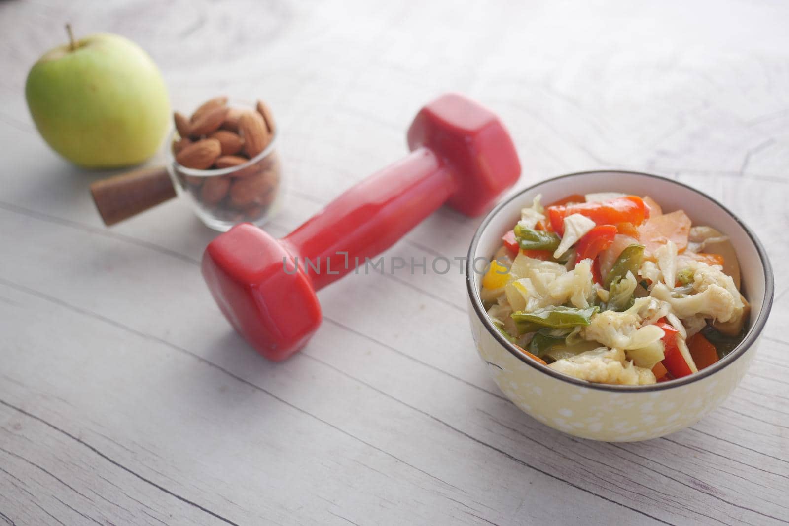 Fitness concept with dumbbell, fresh vegetable , almond and apple on table .