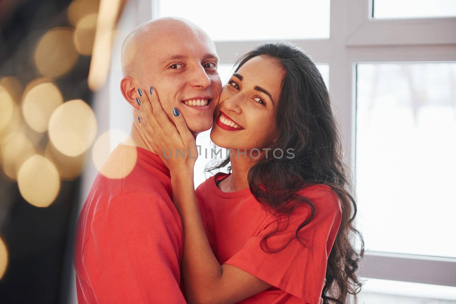 Feels awesome to be together. Cheerful couple standing near the window, smiling and looking into the camera.