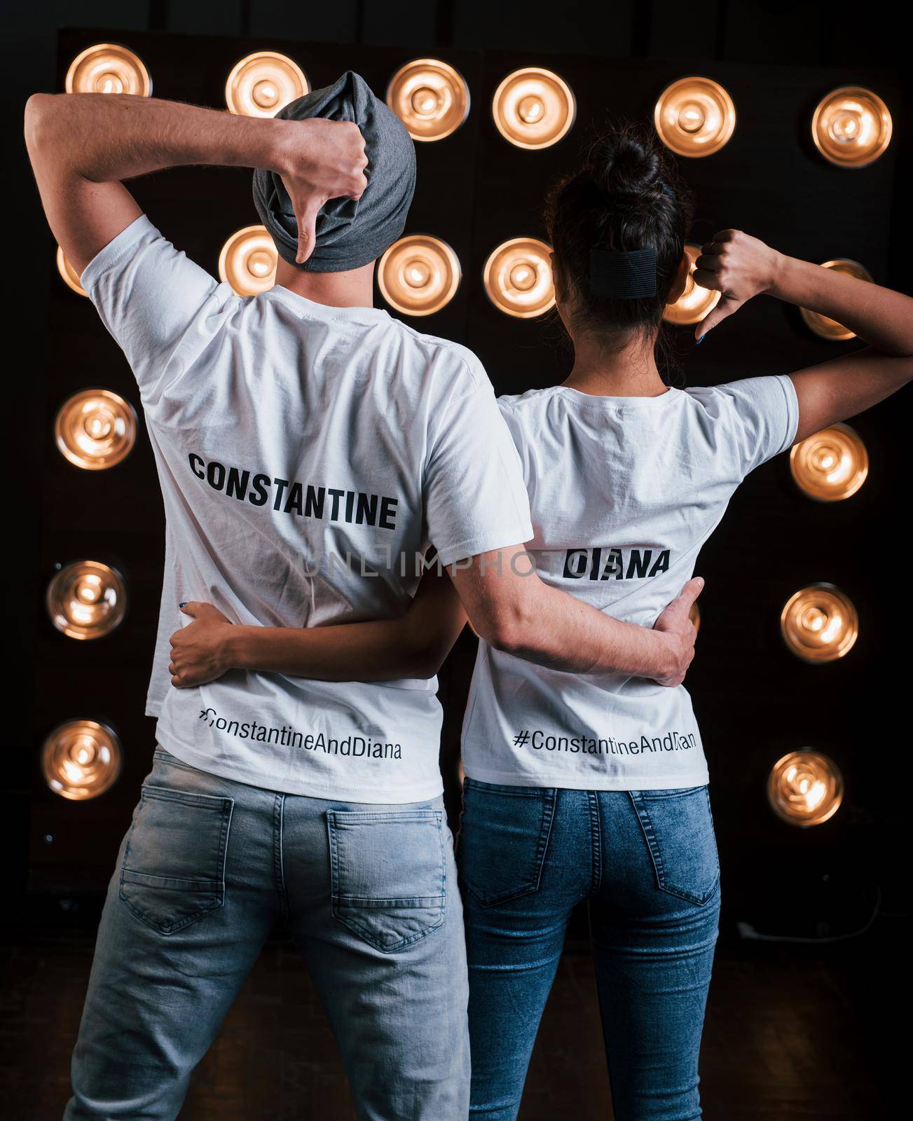 Gestures with thumbs up and hugs. Back view of couple in shirts with their names on it standing next to studio lights.