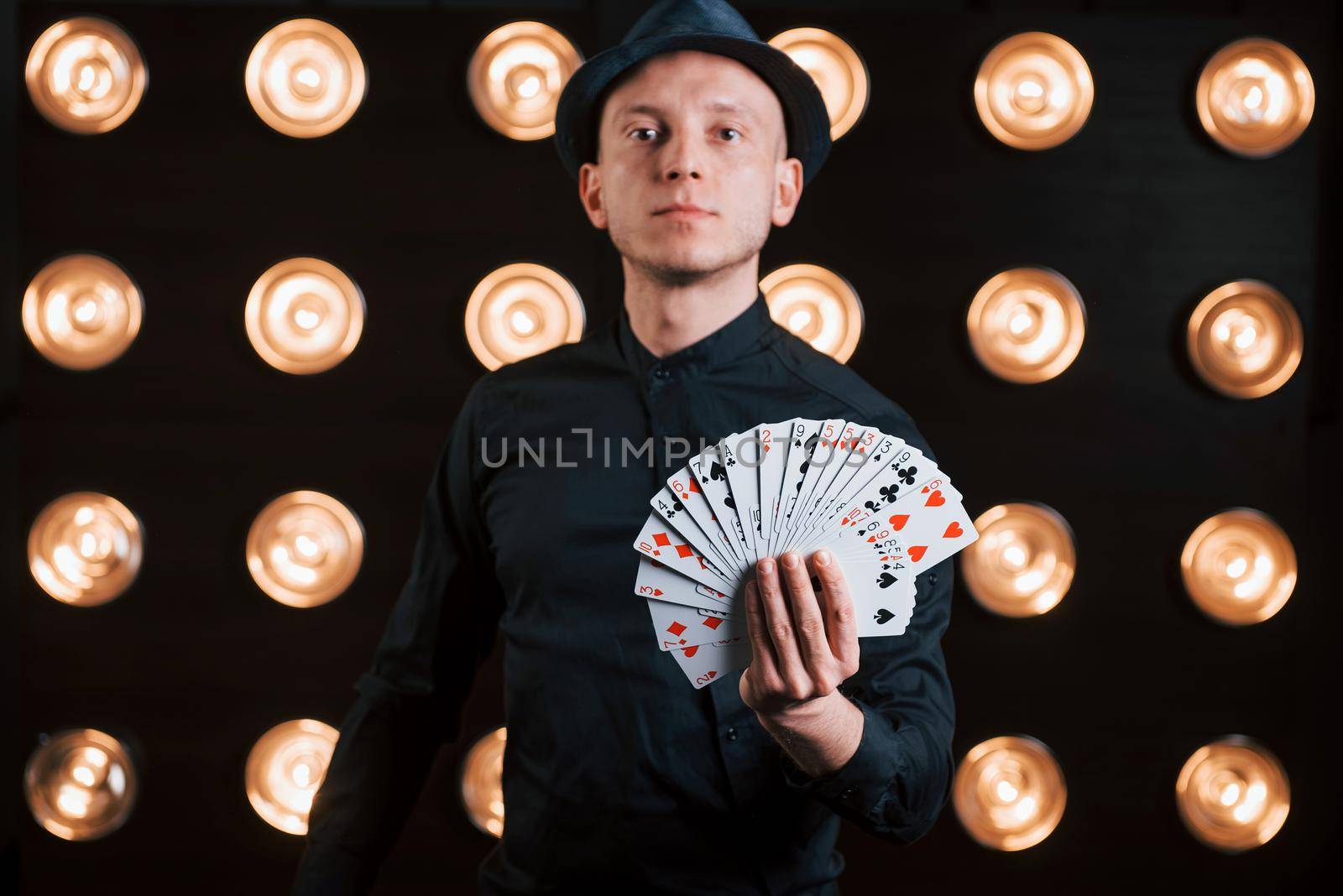 Just pick your card. Magician in black suit standing in the room with special lighting at backstage.