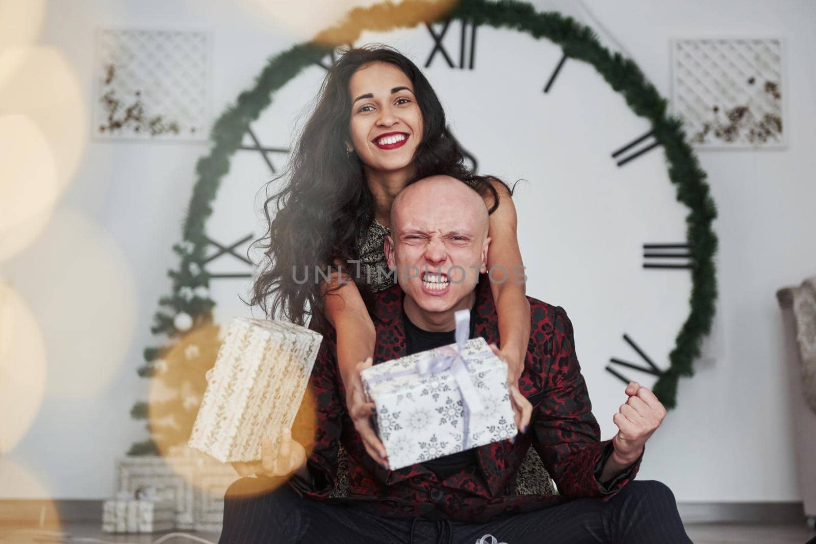 Guy finally gets his gift. Couple in the holiday clothes. Big watch at background. Five minutes to New year.