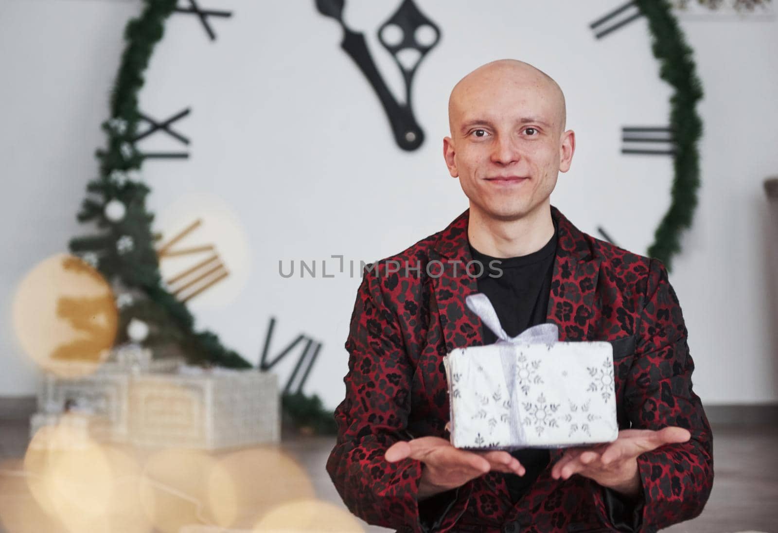 This present is for you. Man with big clock behind him sitting with New year gift boxes in holiday clothings.