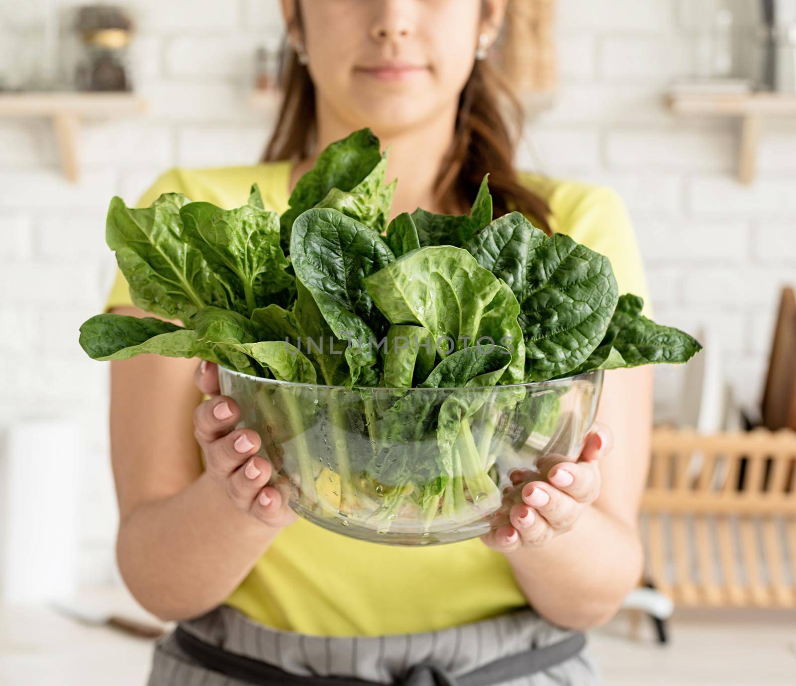 Preparing healthy foods. Healthy eating and dieting. Young caucasian brunette woman holding a bowl of fresh spinach in the kitchen