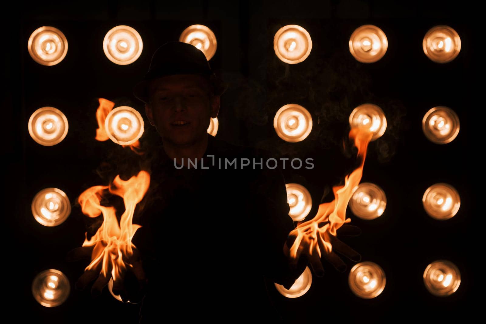 Dangerous beauty of the fire in the hands. Professional magician showing trick. Light bulbs on background.