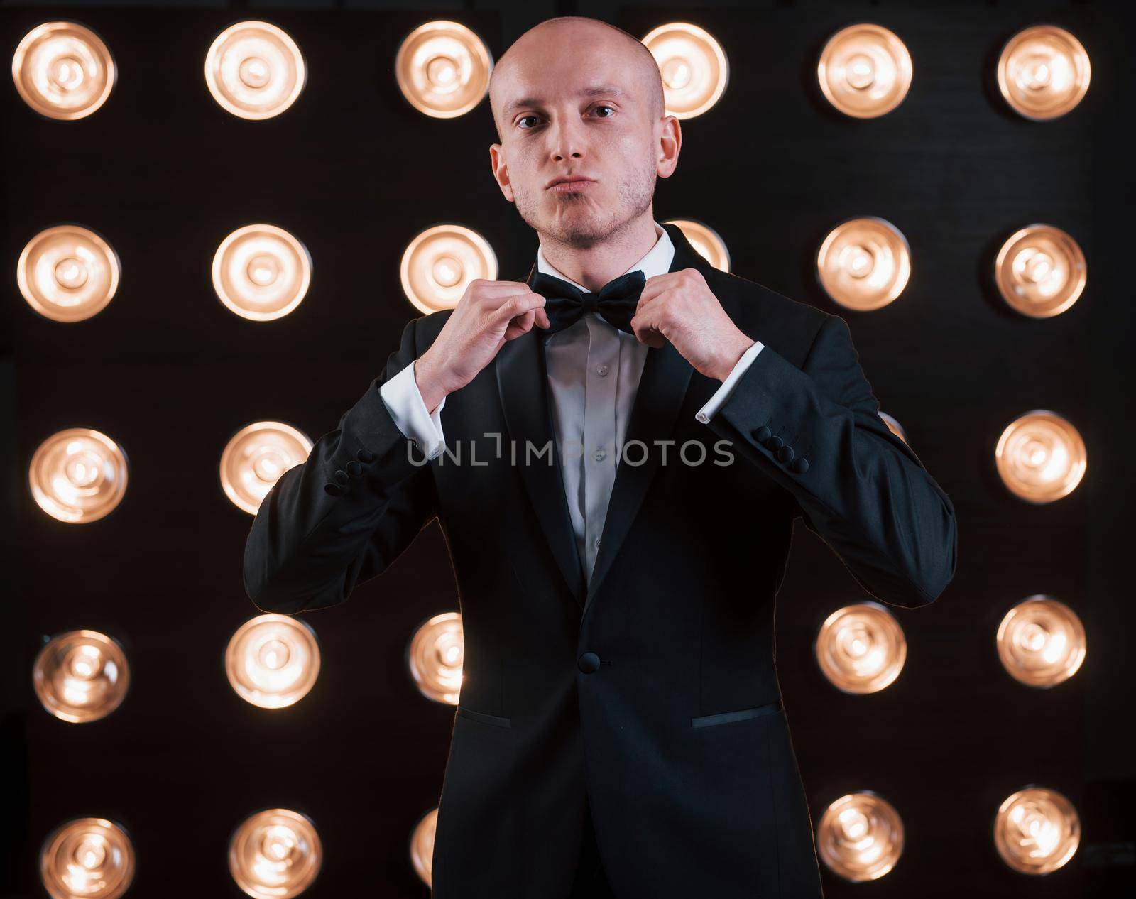 Adjusts the tie. Ready for the show. Magician in black suit standing in the room with special lighting at backstage.