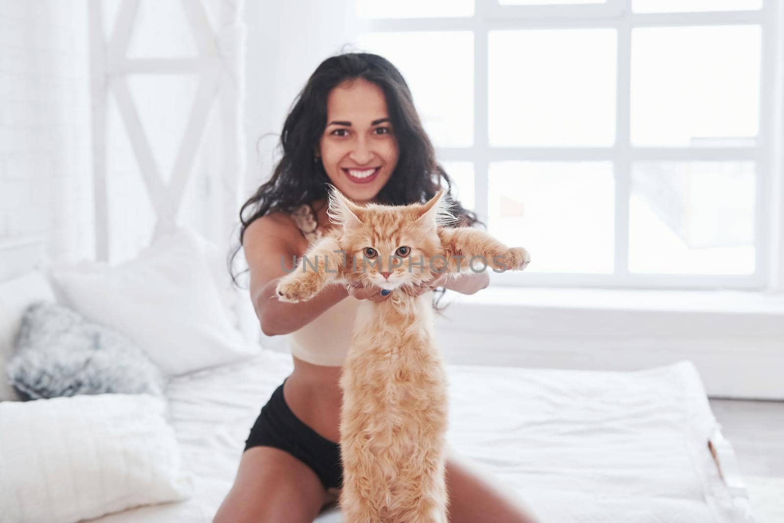 Girl holding her favourite cat. Attractive blonde resting on the white bed with her cute kitten.