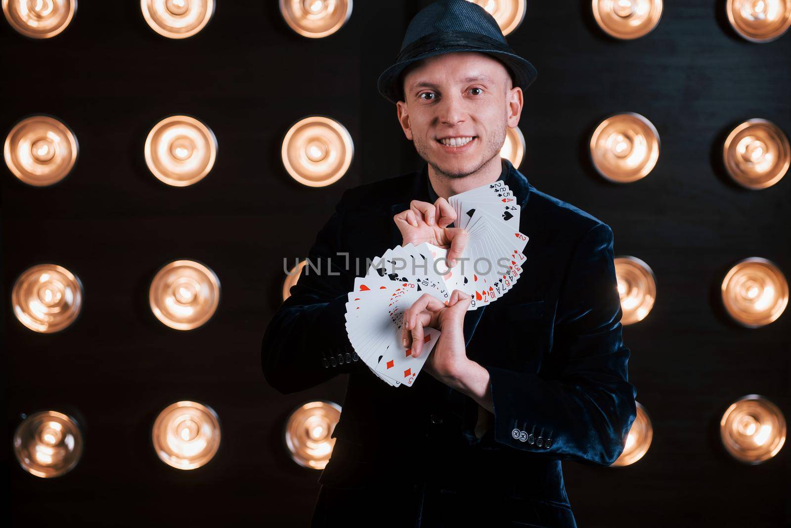 Your turn to pick. Magician in black suit and with playing cards standing in the room with special lighting at backstage.