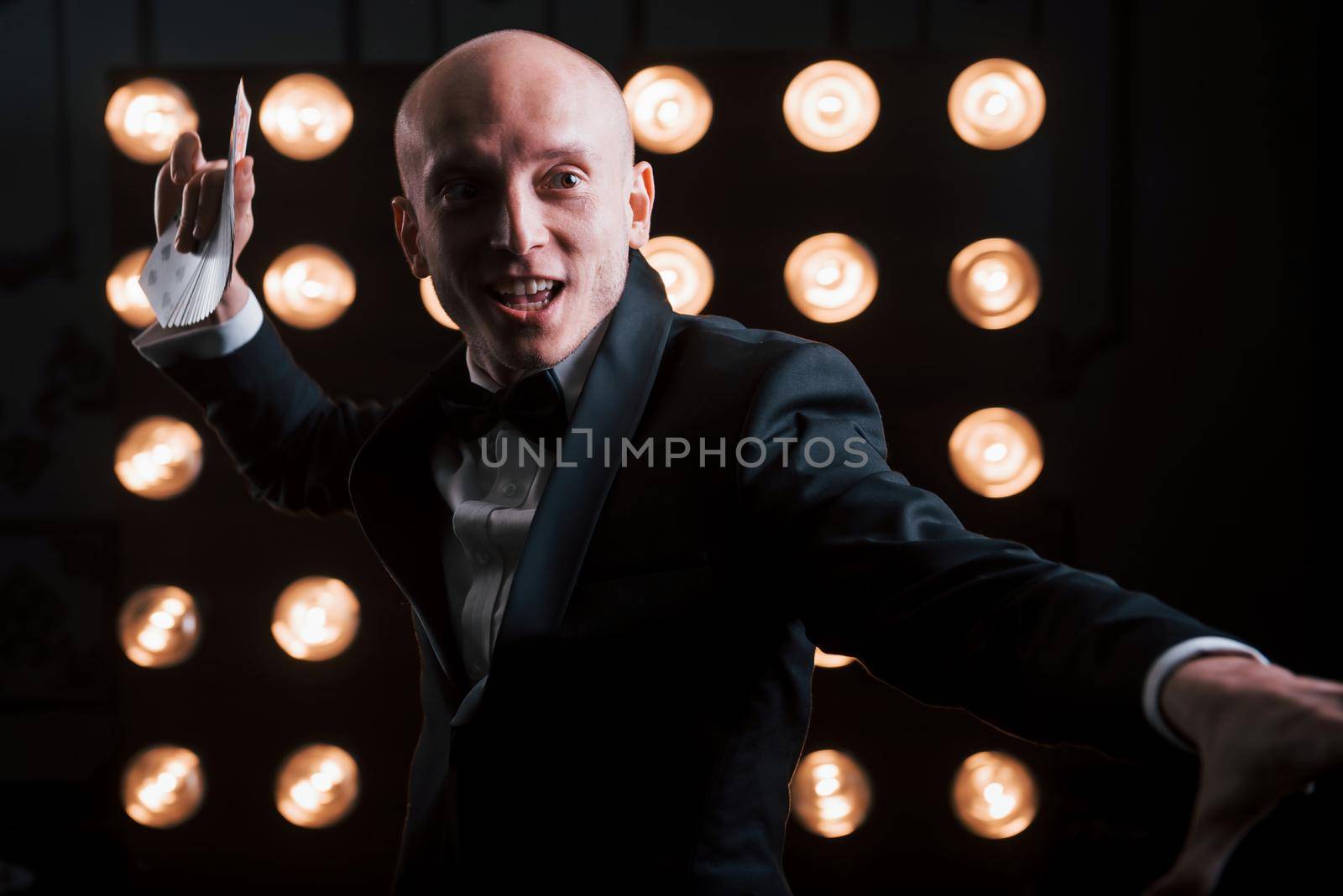 Throwing-like move. Magician in black suit and with playing cards standing in the room with special lighting at backstage.