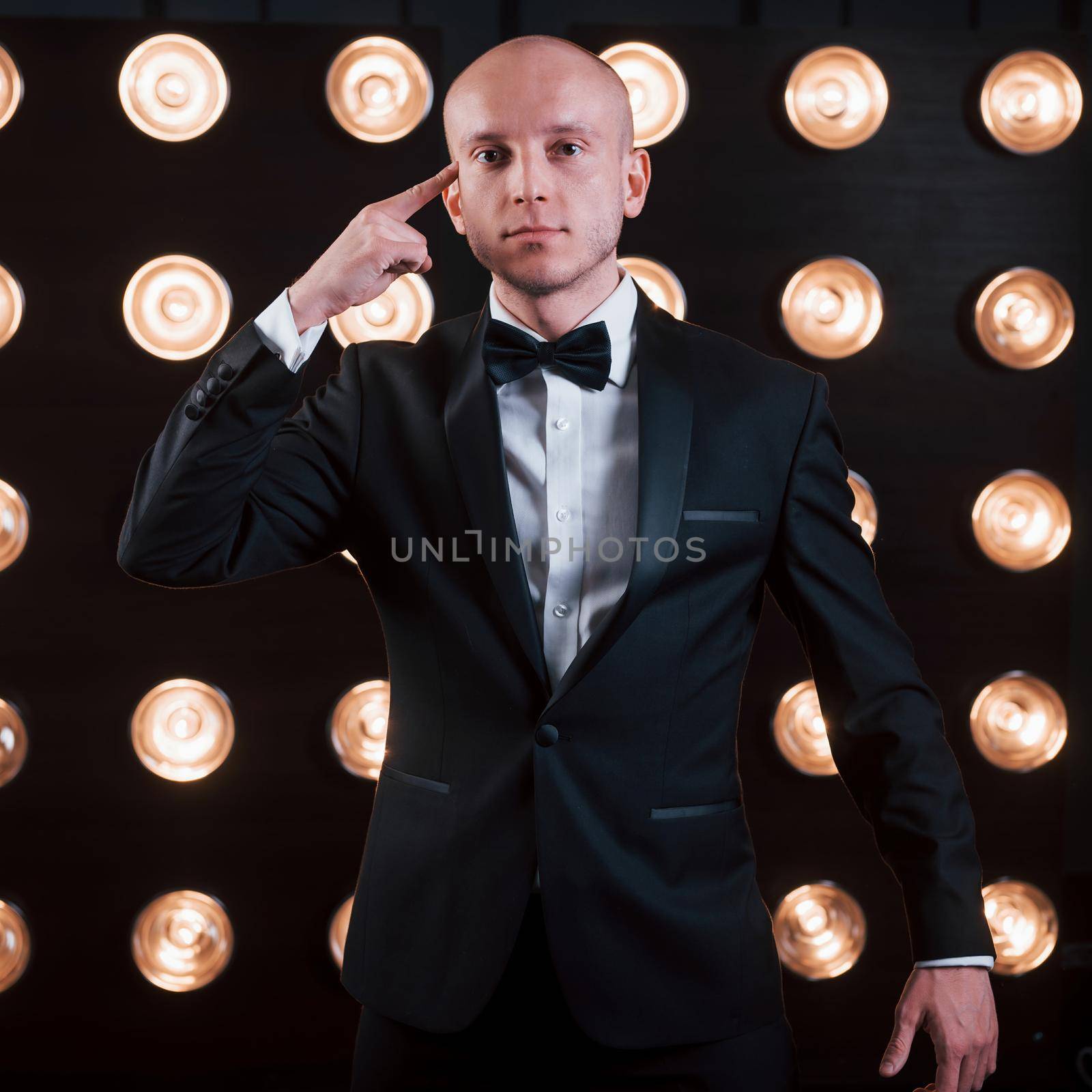 Trying to read your mind. Magician in black suit standing in the room with special lighting at backstage.