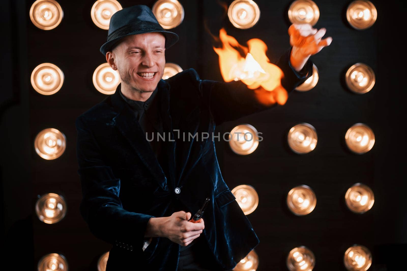 Professional magician showing trick and playing with fire. Light bulbs on background.