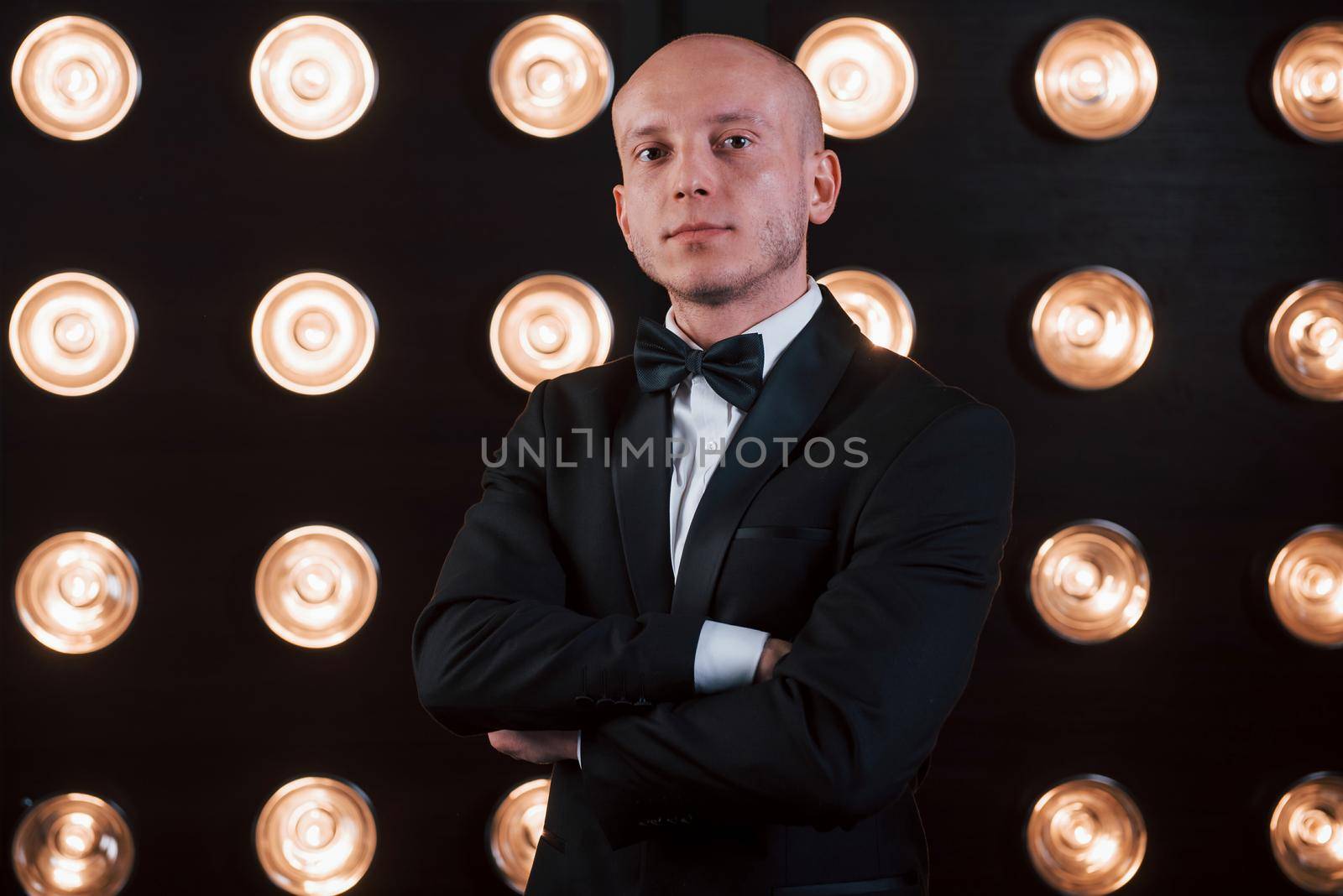 Nice portrait of professional illusionist. Magician in black suit standing in the room with special lighting at backstage.