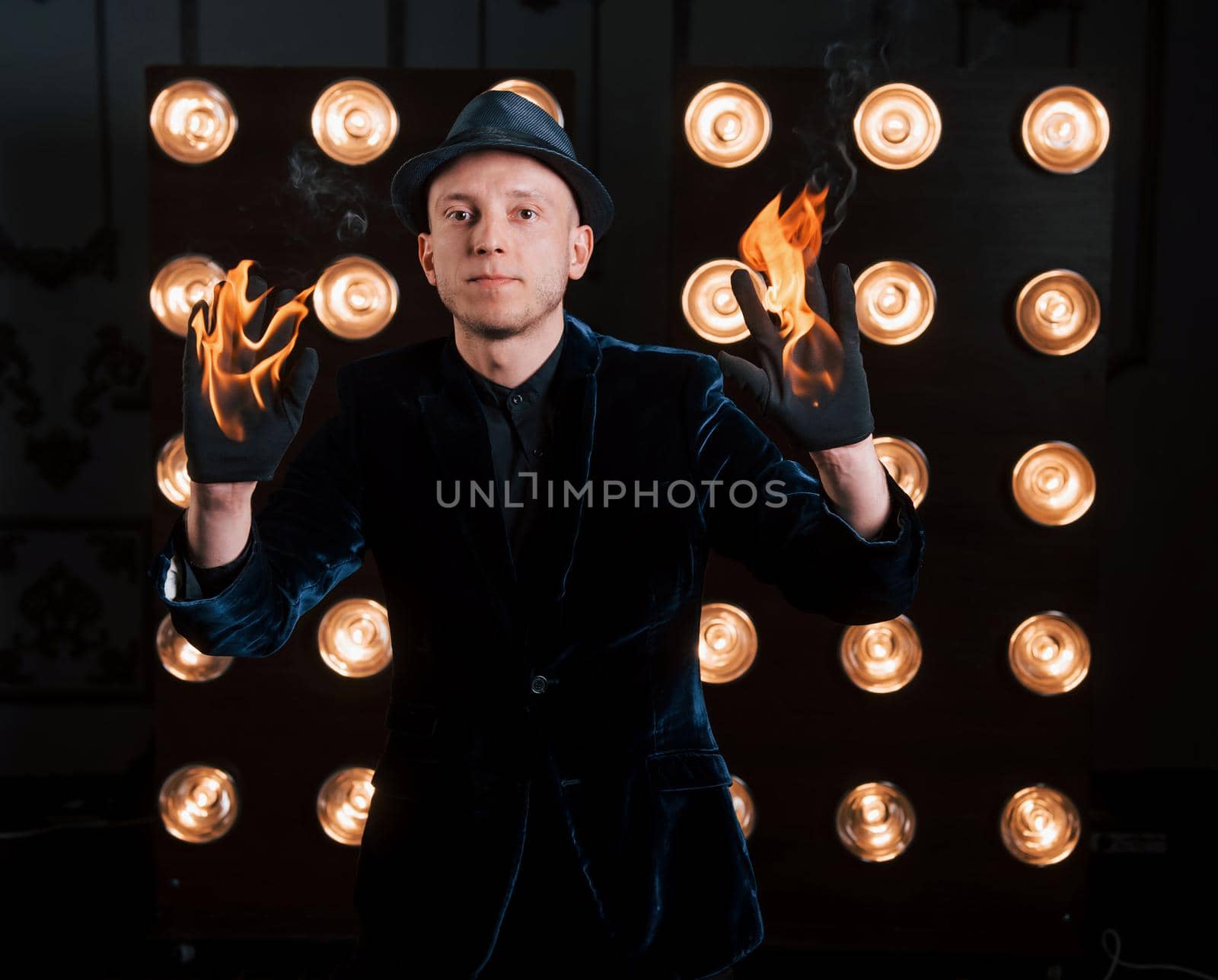 Hands is burning but this is no big deal for this magician. Professional illusionist in black hat, shirt and gloves playing with fire.